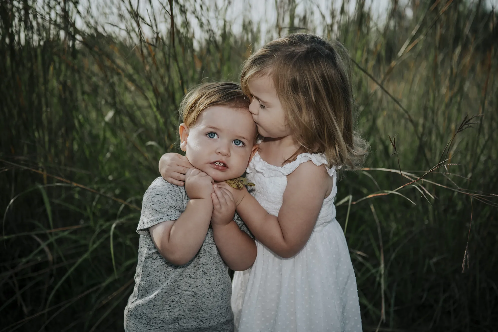Family photos in the Cedar Valley, big sister kissing her little brother