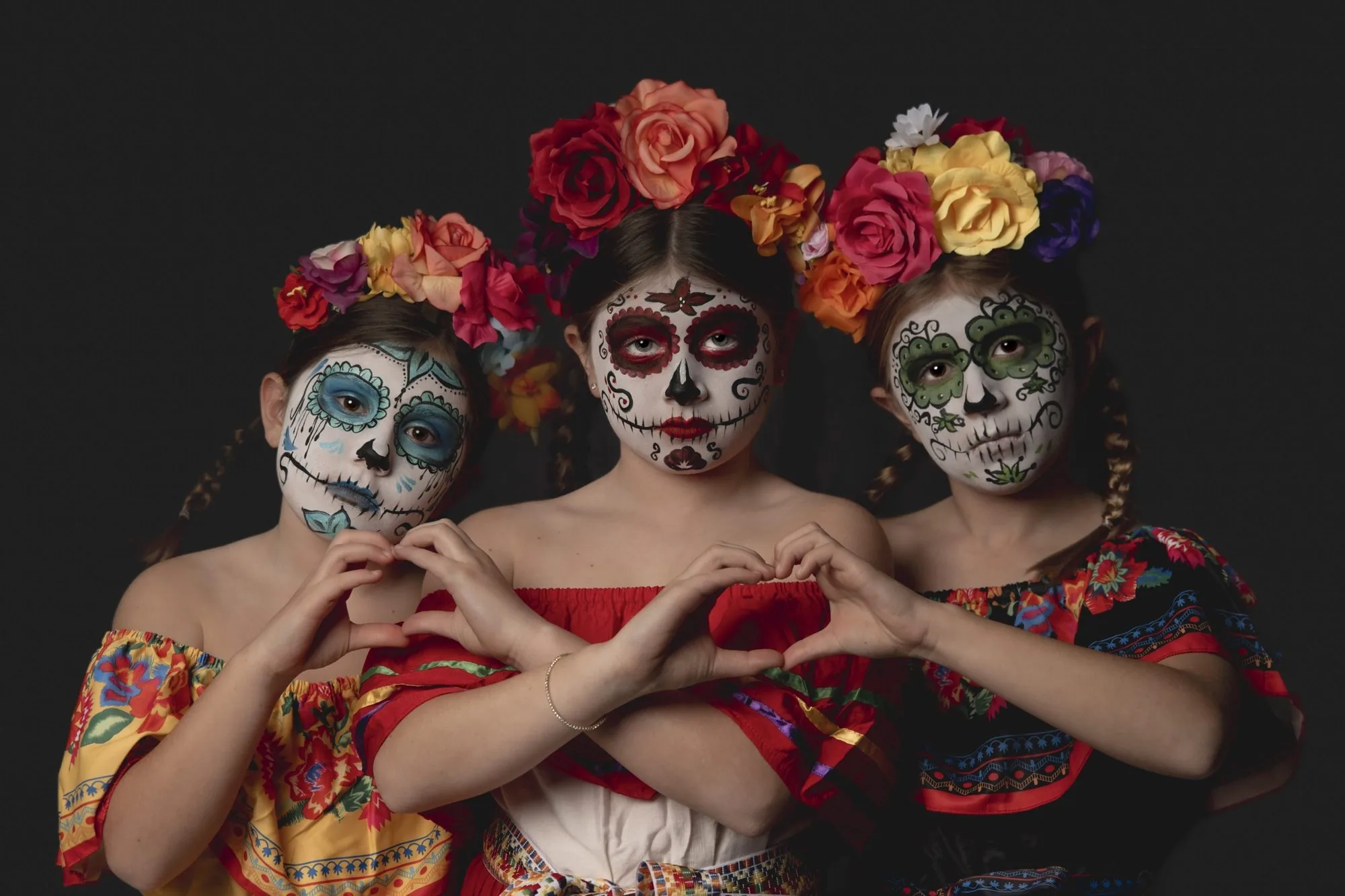 Three girls in sugar skull makeup and flower crowns making heart hands at a Cedar Falls studio Halloween session