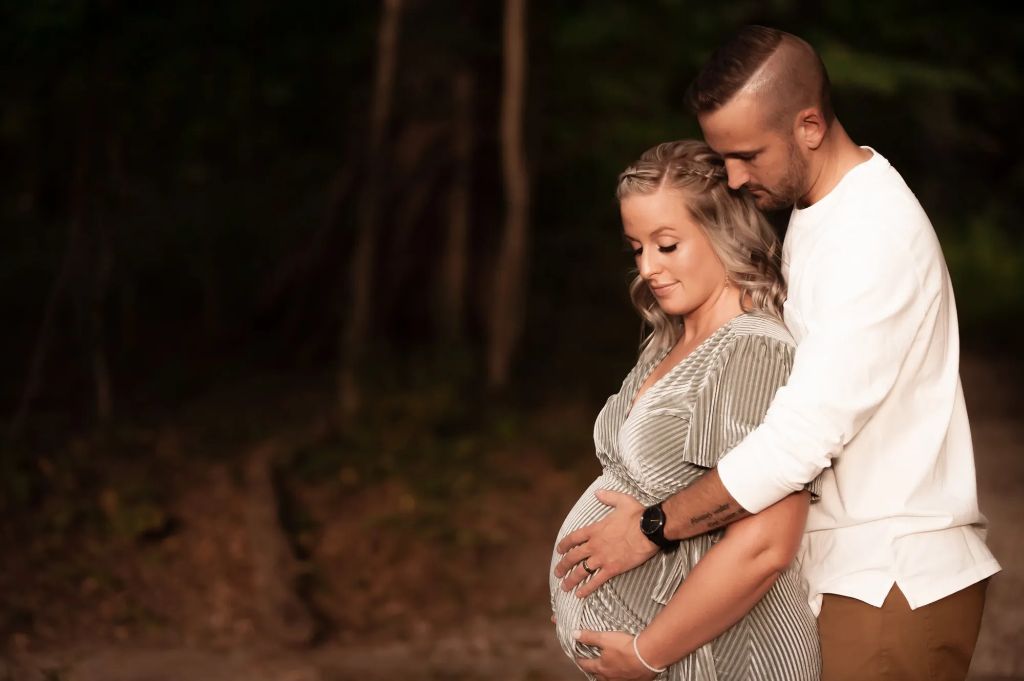 Maternity photos in the Cedar Valley, couple embracing in the woods