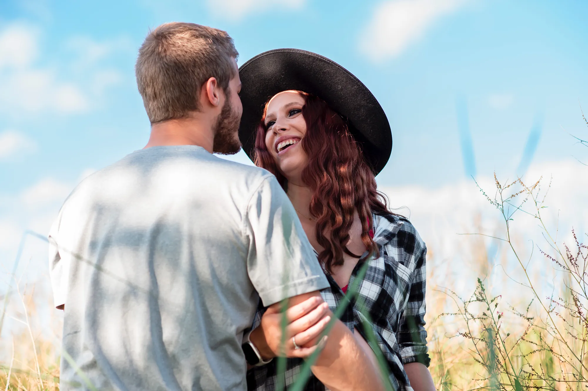 Maternity photos in the Cedar Valley, couple laughing in a summer field