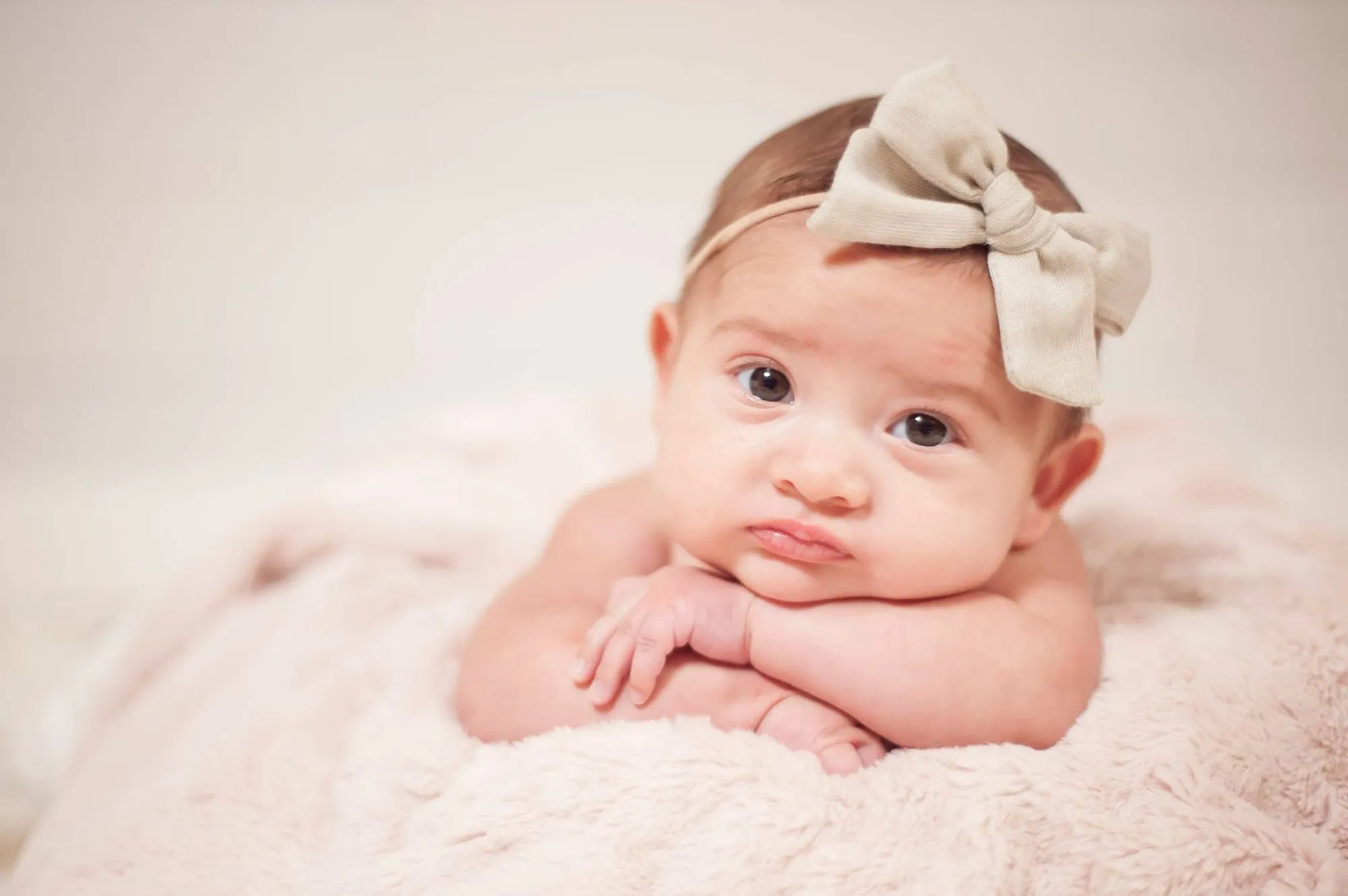 Newborn photos in the Cedar Valley, baby girl with a cream bow on a soft pink blanket