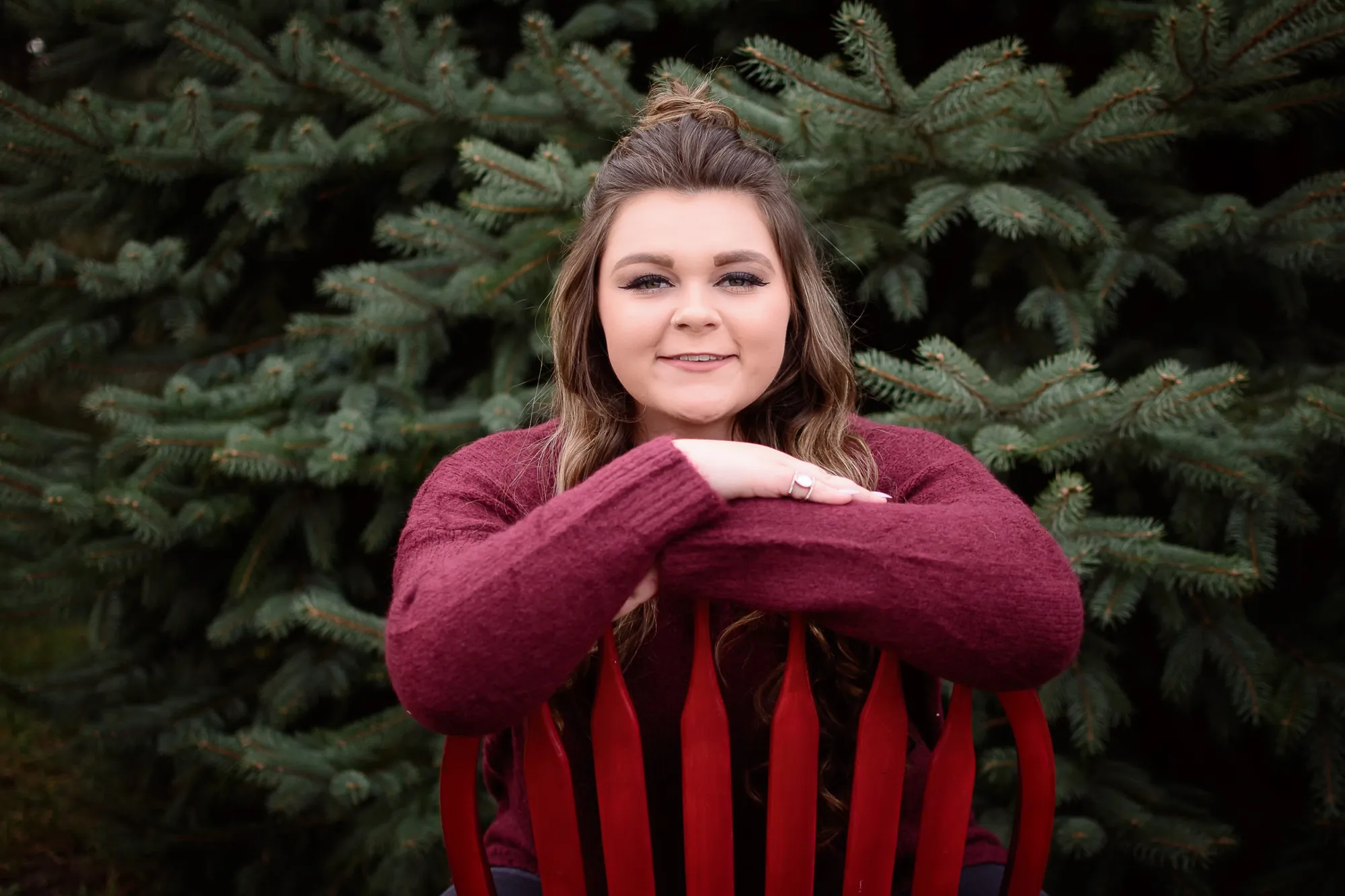 Senior pictures in the Cedar Valley, red chair in front of evergreen trees