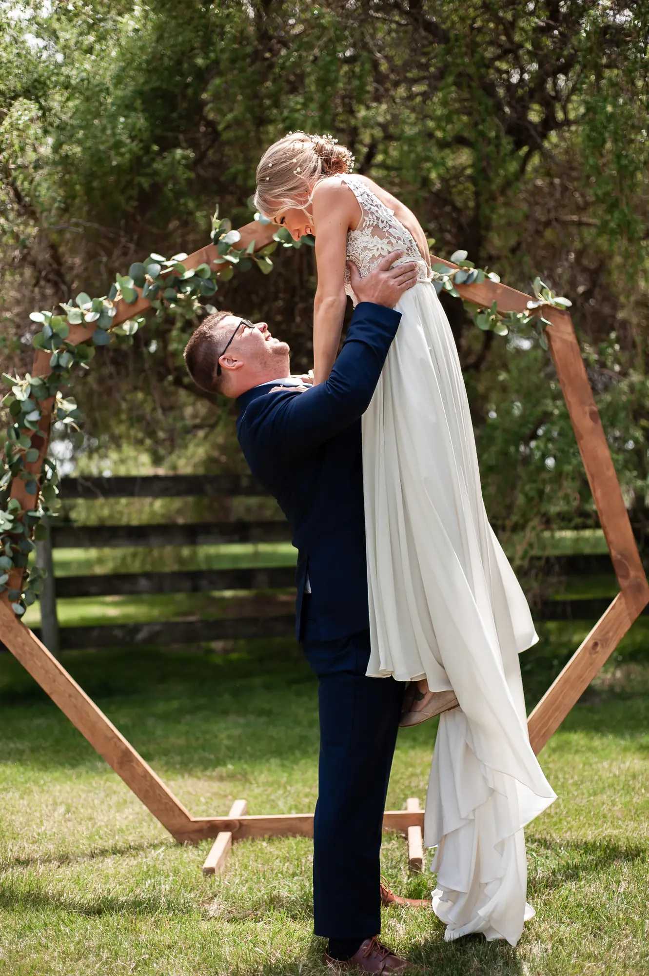 Wedding photography in the Cedar Valley, groom lifting the bride at the ceremony arch