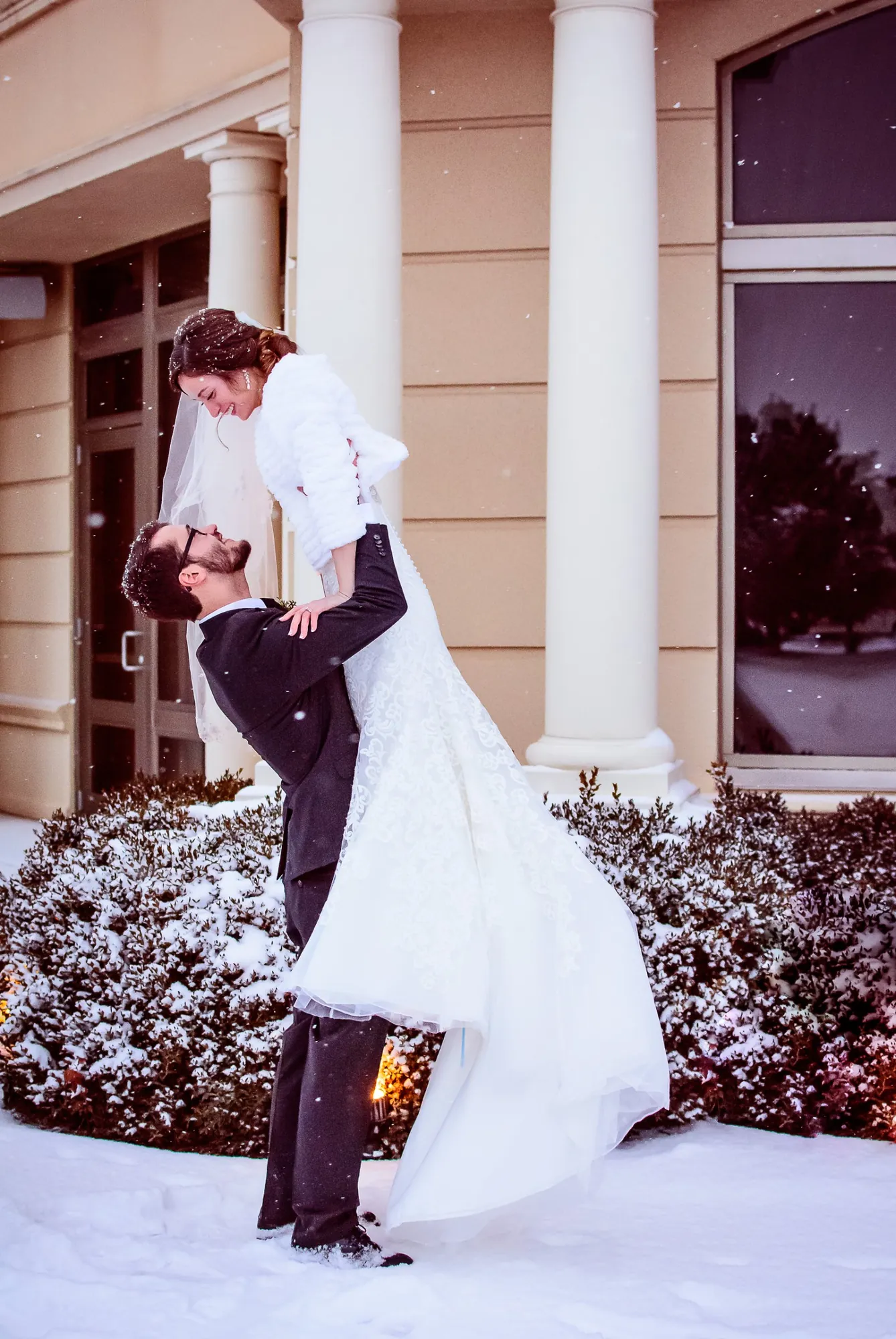 Winter wedding photography in the Cedar Valley, groom lifting the bride in falling snow